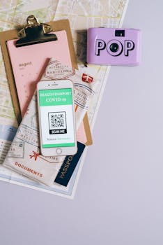 Flat lay of travel essentials with smartphone health passport, camera, map, and documents.